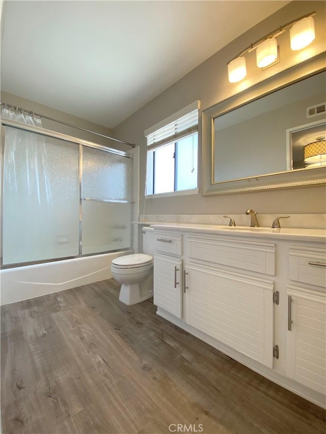 full bathroom featuring visible vents, toilet, wood finished floors, combined bath / shower with glass door, and vanity