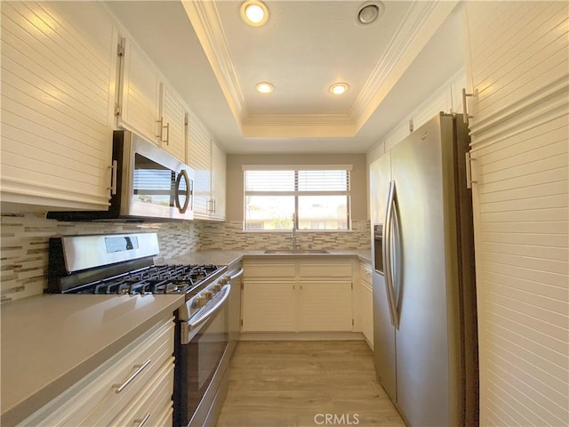 kitchen featuring tasteful backsplash, appliances with stainless steel finishes, a tray ceiling, crown molding, and a sink