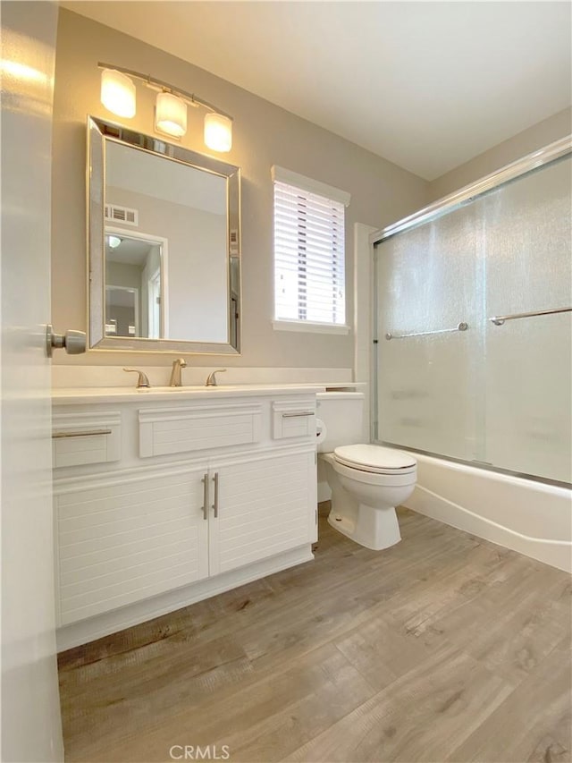 bathroom featuring bath / shower combo with glass door, visible vents, toilet, vanity, and wood finished floors