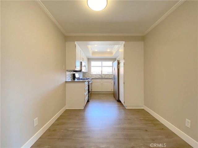 kitchen with stainless steel appliances, white cabinetry, light wood-style floors, a raised ceiling, and crown molding