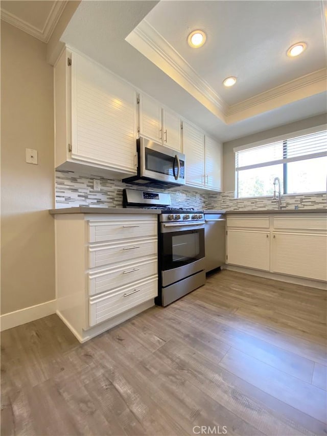 kitchen featuring a raised ceiling, decorative backsplash, stainless steel appliances, crown molding, and light wood-type flooring