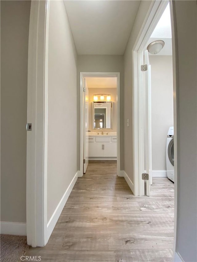 hallway featuring light wood-type flooring, washer / dryer, and baseboards