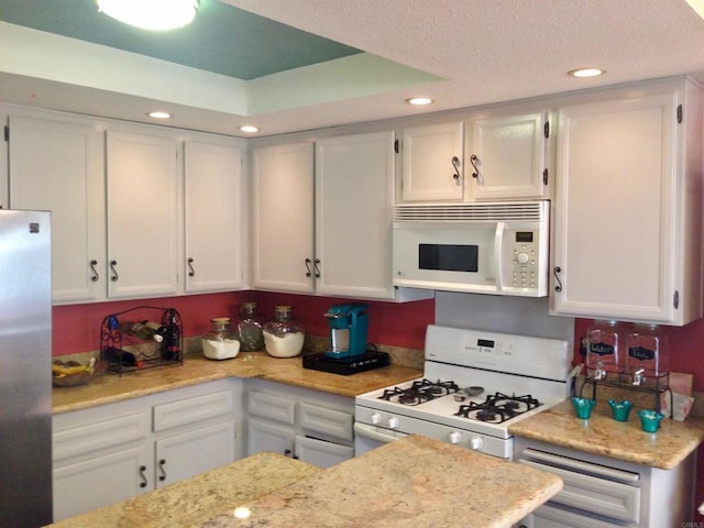 kitchen with white cabinetry, light stone counters, white appliances, and a textured ceiling