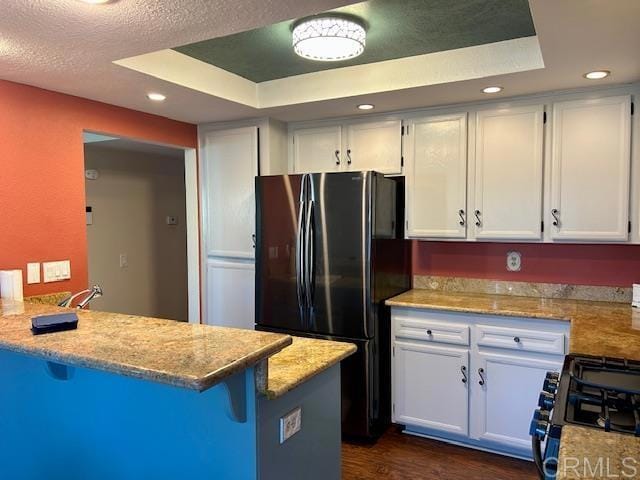 kitchen with freestanding refrigerator, white cabinetry, a tray ceiling, and gas range