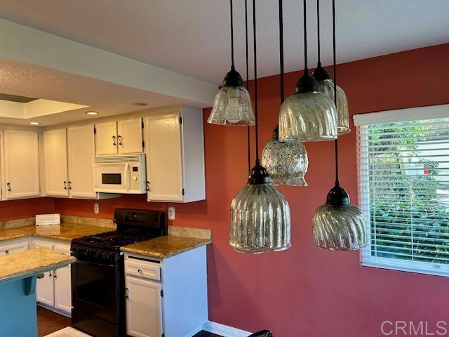 kitchen featuring white microwave, light stone countertops, white cabinets, and black gas range oven