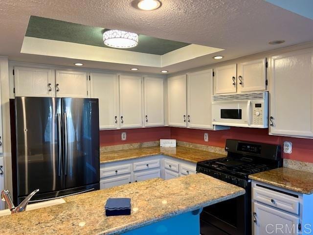 kitchen with a textured ceiling, white microwave, range with gas stovetop, freestanding refrigerator, and a tray ceiling