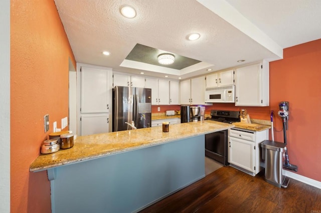 kitchen with dark wood-style floors, a raised ceiling, appliances with stainless steel finishes, white cabinets, and a peninsula