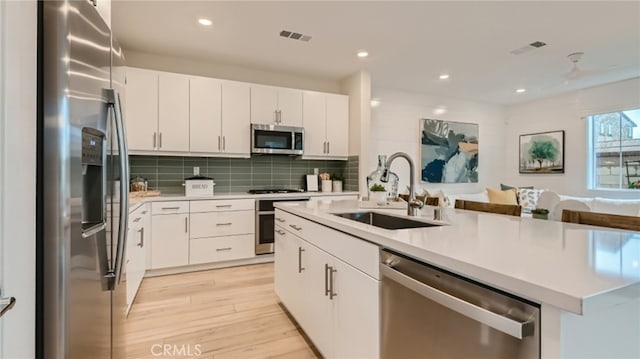 kitchen with sink, white cabinets, stainless steel appliances, a center island with sink, and light wood-type flooring