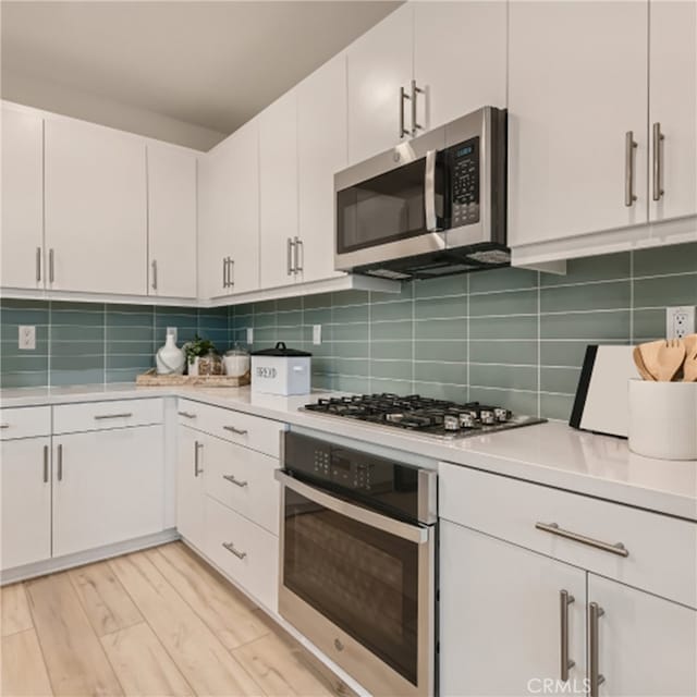 kitchen with backsplash, light wood-type flooring, white cabinets, and appliances with stainless steel finishes