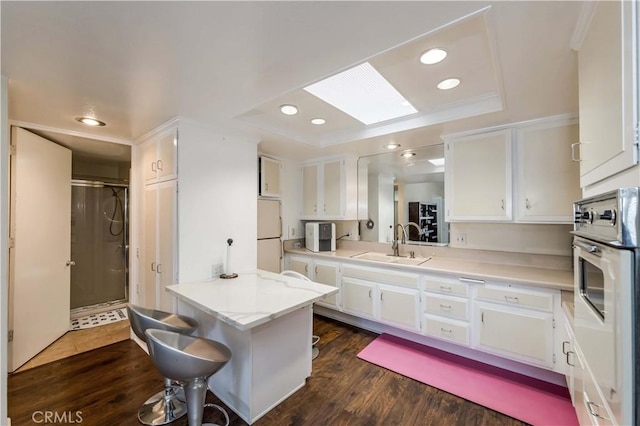 kitchen featuring white cabinetry, sink, white appliances, and a skylight