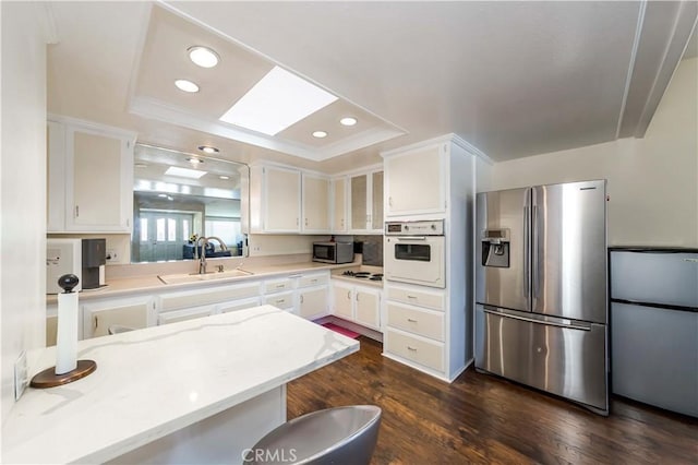 kitchen featuring sink, appliances with stainless steel finishes, dark hardwood / wood-style floors, a raised ceiling, and white cabinets