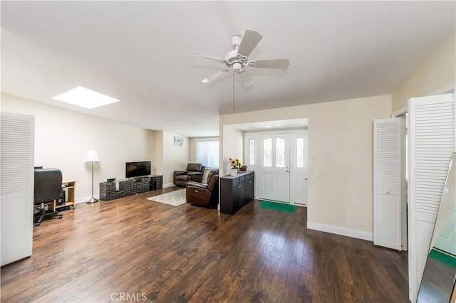 living room with dark wood-type flooring, ceiling fan, and a skylight