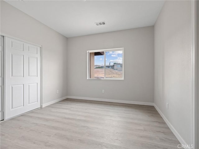 unfurnished room featuring visible vents, light wood-style flooring, and baseboards