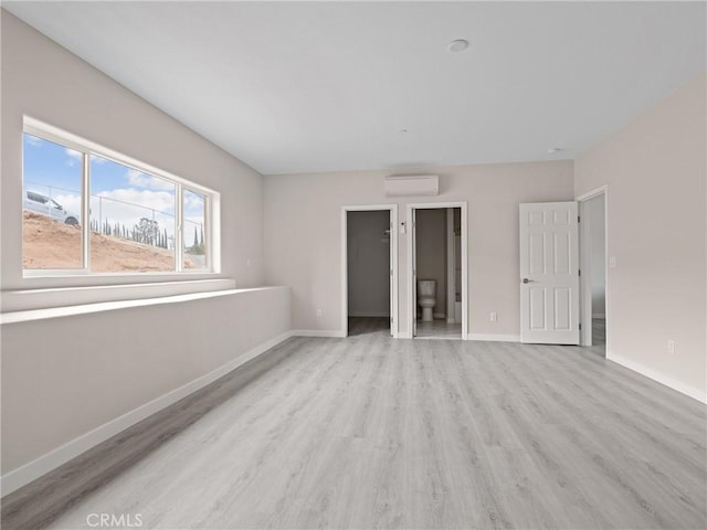 unfurnished bedroom with light wood finished floors, a spacious closet, a wall mounted AC, and baseboards