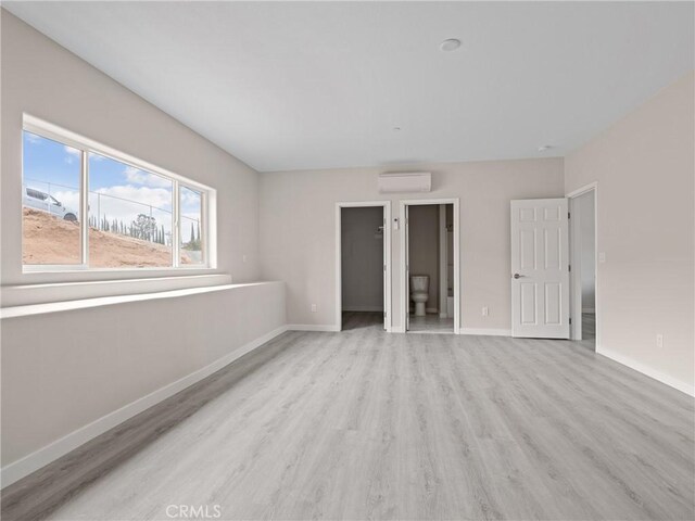 8411 Buckthorn Ave, Hesperia, CA 92345 - unfurnished bedroom with a wall mounted AC, light wood-type flooring, baseboards, and a walk in closet