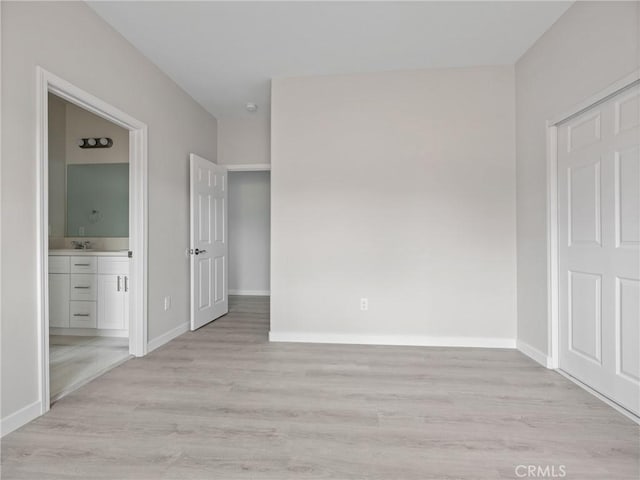 unfurnished bedroom featuring a sink, connected bathroom, baseboards, and light wood-style floors