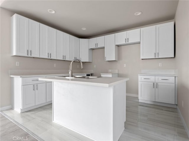 kitchen featuring a kitchen island with sink, white cabinets, baseboards, and a sink