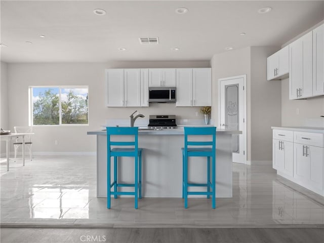 kitchen featuring visible vents, light countertops, appliances with stainless steel finishes, a kitchen breakfast bar, and white cabinets