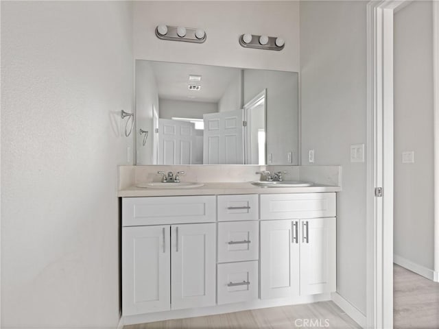 full bathroom featuring double vanity, wood finished floors, baseboards, and a sink