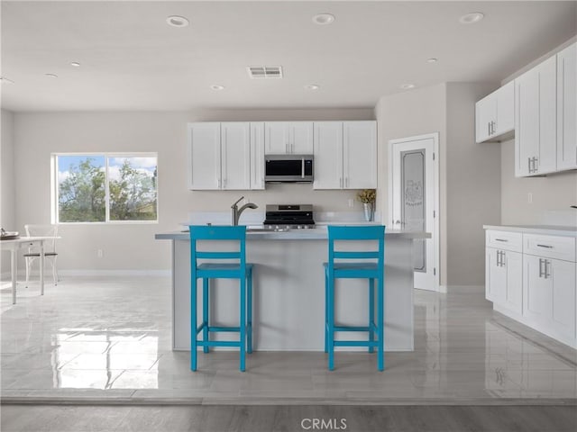 kitchen with visible vents, a kitchen bar, appliances with stainless steel finishes, white cabinets, and light countertops