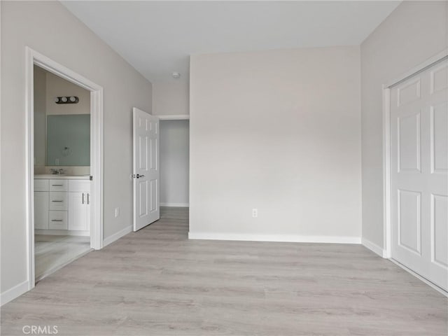 unfurnished bedroom featuring ensuite bath, light wood-type flooring, baseboards, and a sink