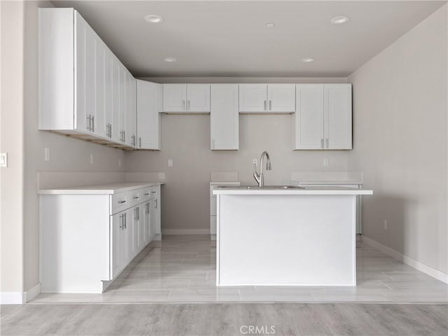 kitchen with a sink, baseboards, a center island with sink, and white cabinetry