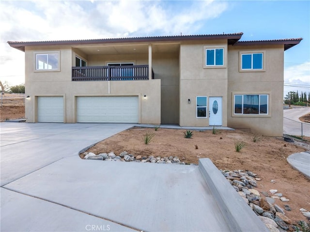 view of property with a garage, stucco siding, driveway, and a balcony