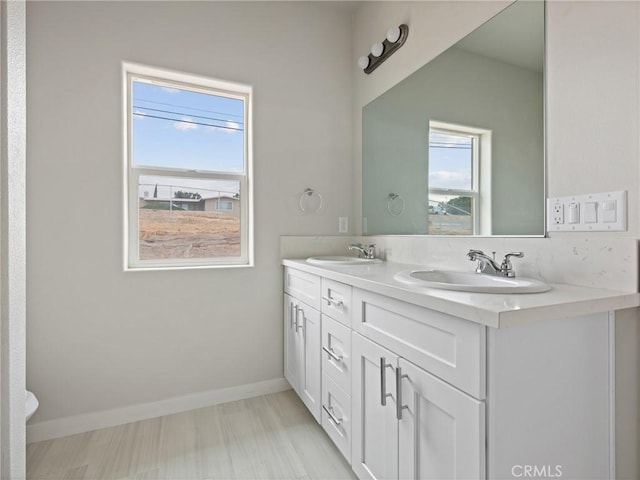 full bath with double vanity, baseboards, and a sink