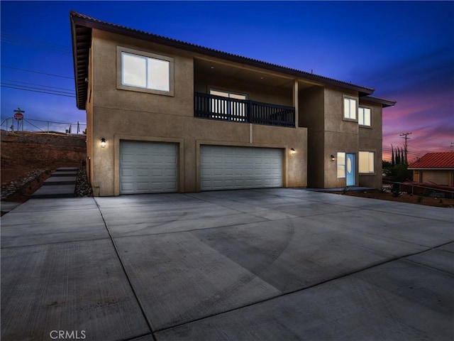 view of front of home featuring concrete driveway, a balcony, an attached garage, and stucco siding