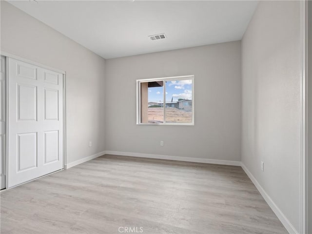 empty room featuring visible vents, baseboards, and light wood-type flooring