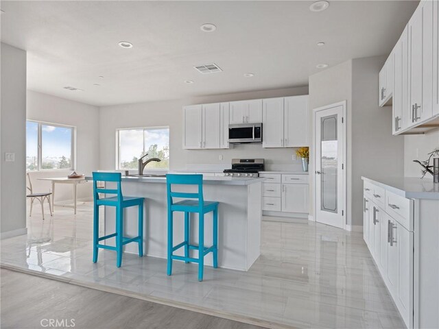 kitchen with light countertops, white cabinets, a kitchen island with sink, and appliances with stainless steel finishes