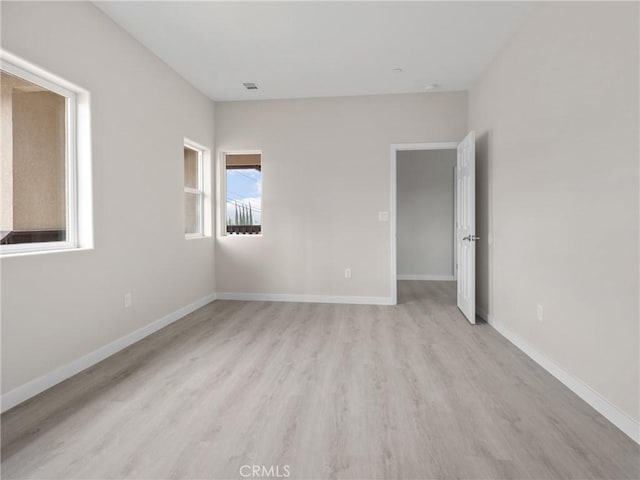 empty room with visible vents, light wood-type flooring, and baseboards