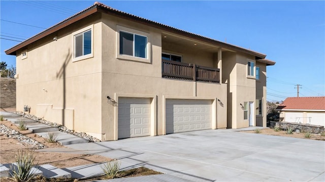 rear view of property featuring stucco siding, a garage, a balcony, and driveway