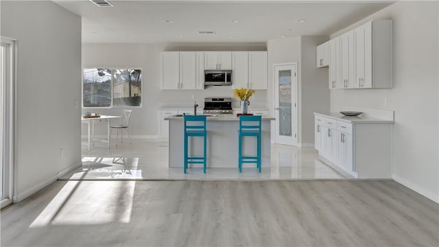 kitchen featuring stainless steel microwave, range, a kitchen island with sink, and white cabinetry