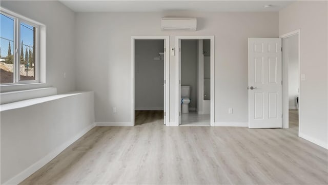 unfurnished bedroom with wood finished floors, baseboards, an AC wall unit, a spacious closet, and a closet