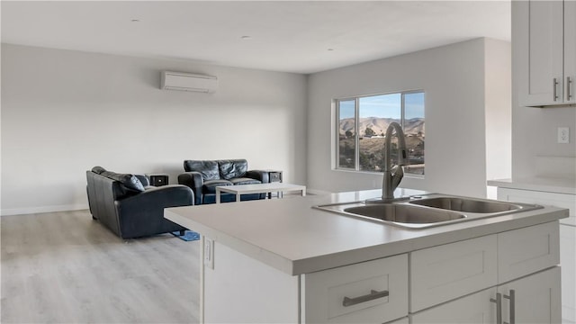 kitchen featuring a center island with sink, a sink, light countertops, a wall mounted air conditioner, and open floor plan