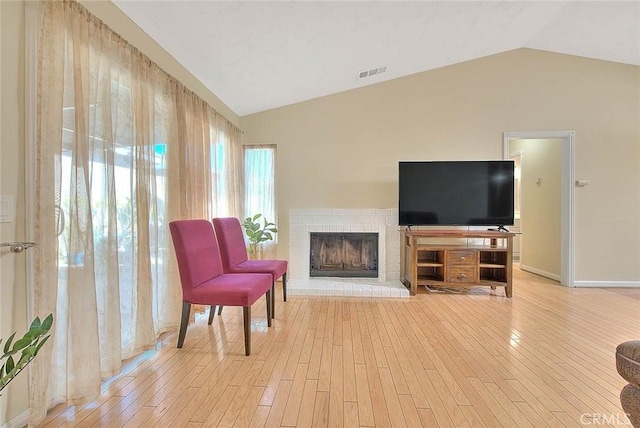 sitting room featuring lofted ceiling, a brick fireplace, visible vents, and light wood-style flooring