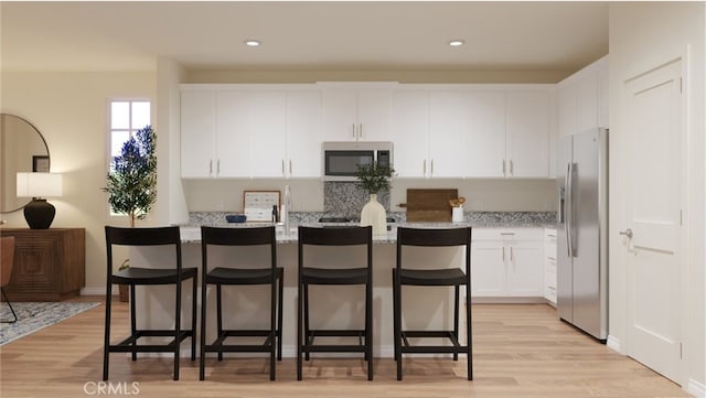 kitchen with appliances with stainless steel finishes, white cabinetry, a kitchen island with sink, light stone countertops, and a kitchen bar