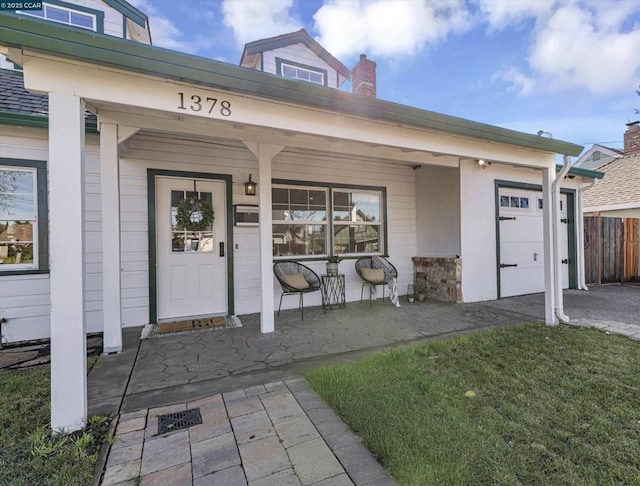 view of exterior entry featuring a porch, a yard, and a garage