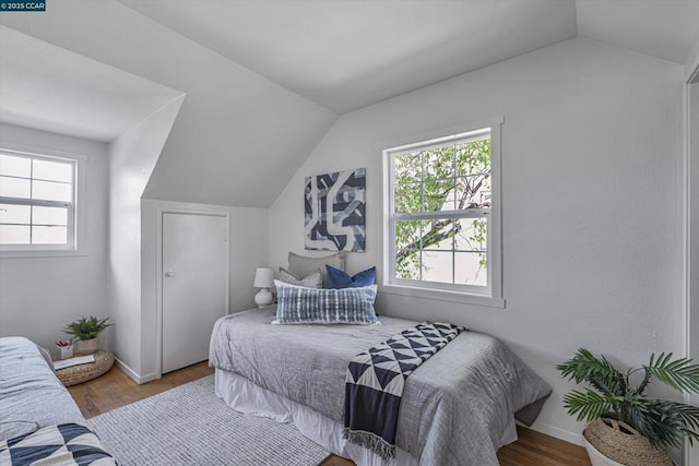 bedroom featuring multiple windows, vaulted ceiling, and wood-type flooring