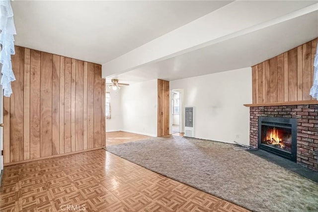 unfurnished living room featuring wood walls, ceiling fan, light parquet flooring, a brick fireplace, and beam ceiling