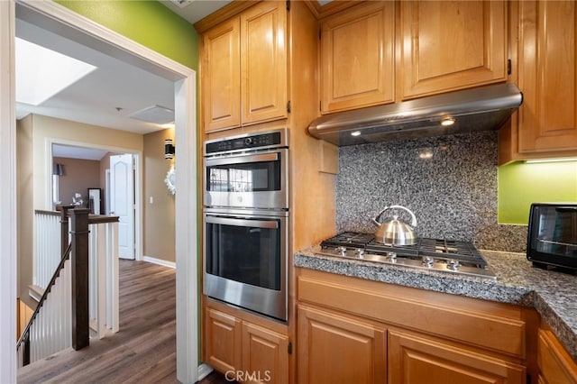 kitchen featuring tasteful backsplash, baseboards, dark wood-type flooring, stainless steel appliances, and under cabinet range hood