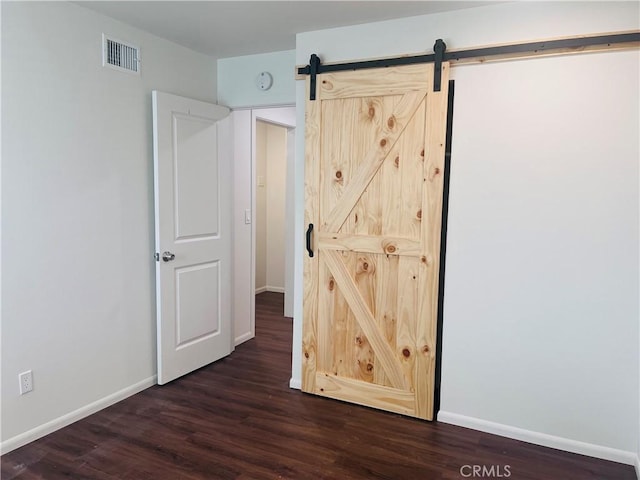 unfurnished bedroom featuring dark wood-type flooring and a barn door