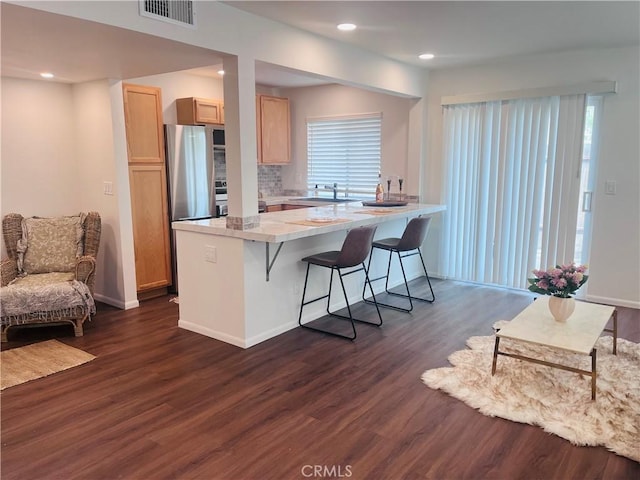 kitchen featuring dark hardwood / wood-style floors, sink, a kitchen bar, decorative backsplash, and light brown cabinets