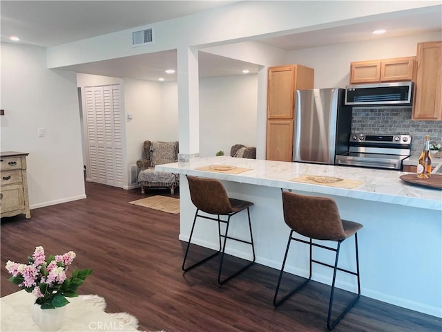 kitchen with appliances with stainless steel finishes, a breakfast bar, light brown cabinets, and dark hardwood / wood-style floors