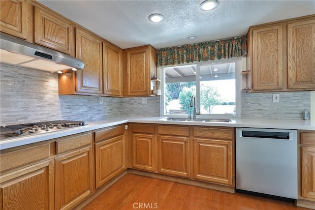 kitchen featuring sink, a textured ceiling, light hardwood / wood-style flooring, stainless steel appliances, and backsplash