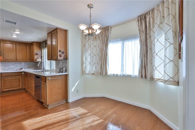 kitchen featuring sink, light wood-type flooring, stainless steel dishwasher, pendant lighting, and decorative backsplash