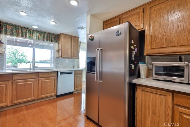 kitchen featuring appliances with stainless steel finishes, sink, light wood-type flooring, backsplash, and a textured ceiling