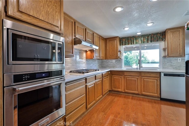 kitchen with sink, light wood-type flooring, backsplash, stainless steel appliances, and a textured ceiling