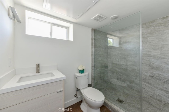 bathroom with a tile shower, a healthy amount of sunlight, vanity, and toilet